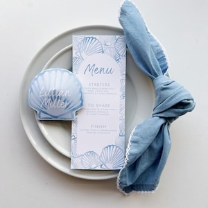 DESCARGAR paquete EDITABLE e IMPRIMIBLE. Tarjeta de lugar con concha costera azul, tarjeta de nombre con vieira azul polvorienta. Menú de cena con concha costera.