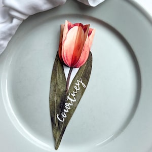 May include: A paper tulip place card with a green stem and leaves. The name "Courtney" is written in white script on the leaf.