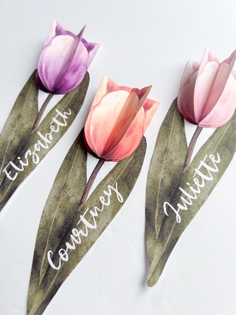 May include: Three paper tulip place cards with green leaves and white calligraphy names: Elizabeth, Courtney, and Juliette.