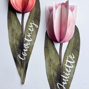 May include: Two watercolour tulip place cards with green leaves and white calligraphy names "Courtney" and "Juliette".