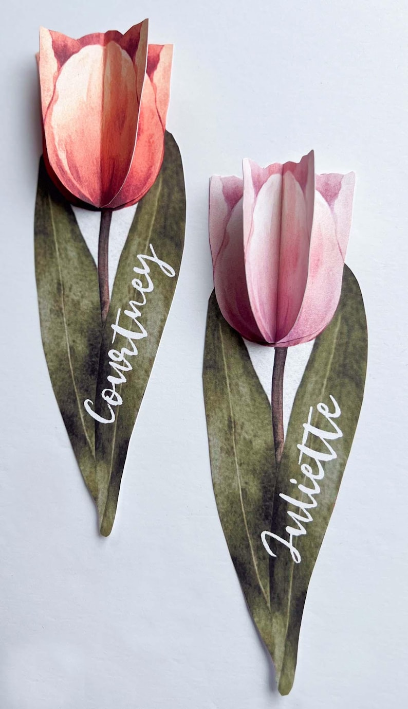 May include: Two watercolour tulip place cards with green leaves and white calligraphy names "Courtney" and "Juliette".