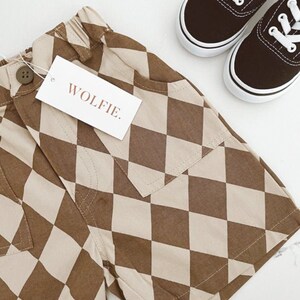 Puede incluir: Shorts de cuadros marrones y beige con un solo bolsillo y una etiqueta que dice "WOLFIE."
