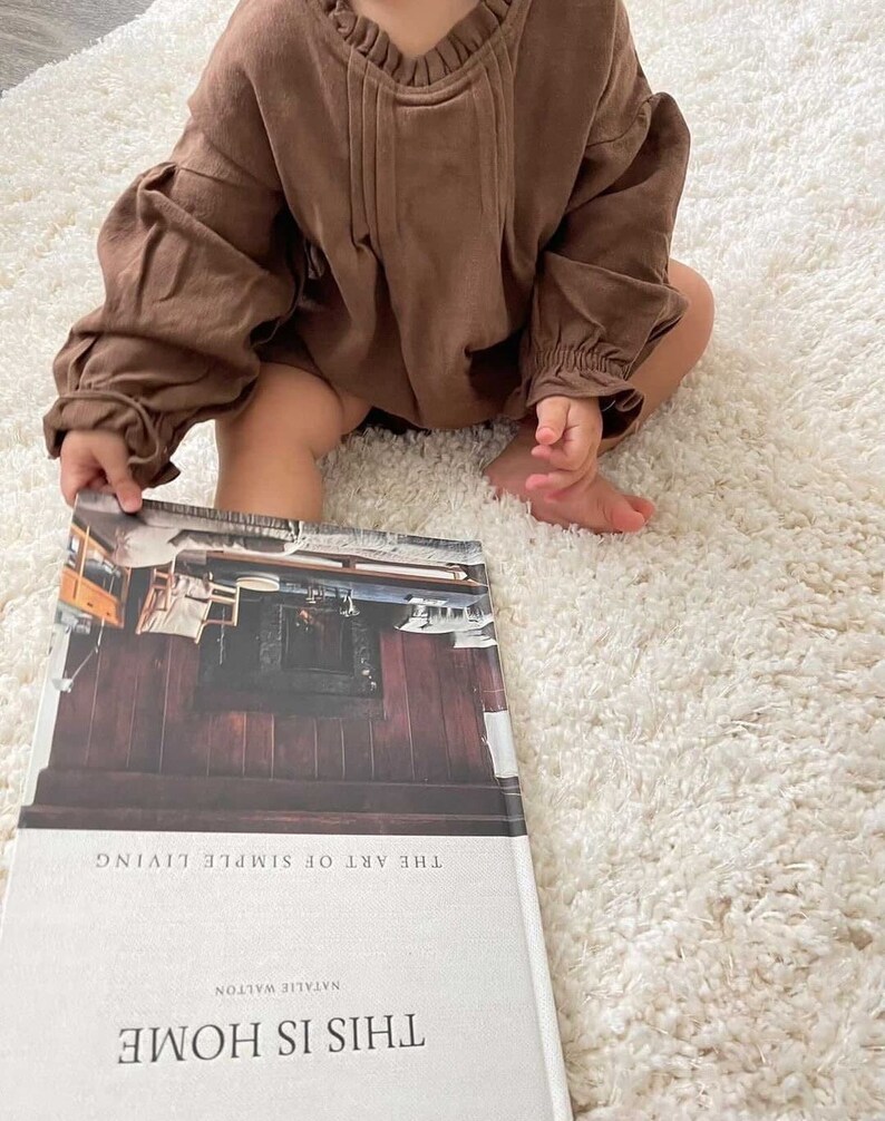 May include: A brown book with the title "This Is Home" and the subtitle "The Art of Simple Living" by Natalie Walton.