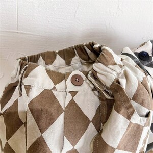 Puede incluir: Pantalones de cuadros marrones y blancos con un bot&oacute;n marr&oacute;n. Los pantalones tienen una cintura con cord&oacute;n y est&aacute;n hechos de una tela suave y c&oacute;moda.