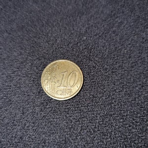 May include: A gold-colored 10 Euro cent coin with the inscription "EURO CENT" and a design of a building.