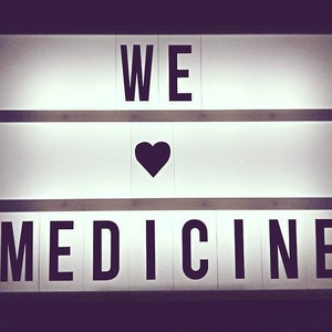Könnte beinhalten: Ein weißes, beleuchtetes Schild mit den Worten "WE ♥ MEDICINE" in schwarzen Buchstaben.