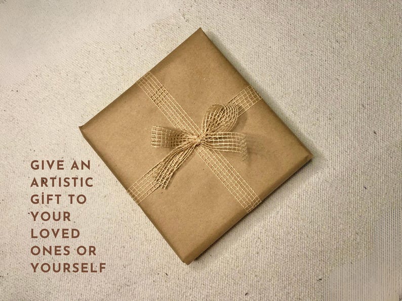 K&ouml;nnte beinhalten: Eine braune Papiert&uuml;te mit einer Schleife aus Naturbast. Auf der T&uuml;te steht der Text "GIVE AN ARTISTIC GIFT TO YOUR LOVED ONES OR YOURSELF".