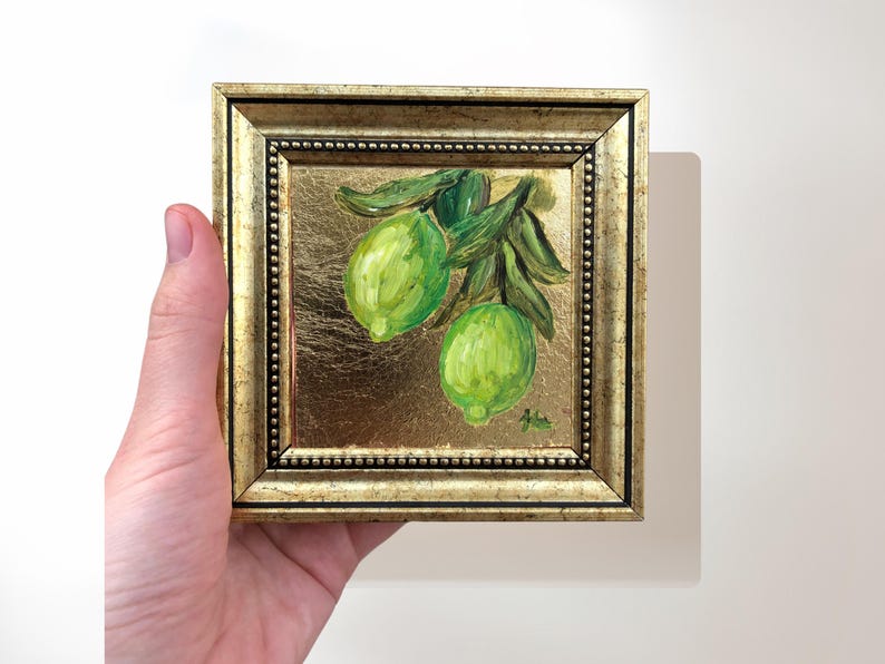 May include: A framed painting of two green limes on a branch with green leaves. The painting is on a gold background.