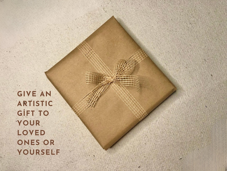 May include: A brown paper gift bag with a natural twine bow. The bag has the text "GIVE AN ARTISTIC GIFT TO YOUR LOVED ONES OR YOURSELF" printed on it.