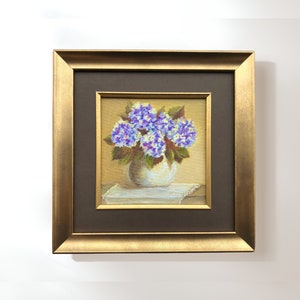 May include: A framed painting depicting a bunch of purple hydrangeas in a white vase. The flowers are arranged simply and elegantly, and the painting is executed in a realistic style.