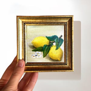 May include: A framed painting of two lemons with green leaves and white flowers on a beige background.
