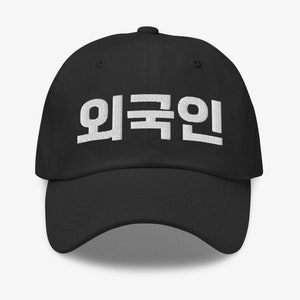 Peut inclure: Casquette de baseball noire avec un texte brodé en blanc qui dit "외국인" en coréen.