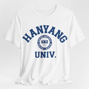 以下が含まれることがあります： 白地に青いハンヤン大学のロゴがプリントされたTシャツ。ロゴは円形のデザインで、大学の名前「Hanyang University」と「1939」が小さなフォントで書かれている。ロゴの下には「UNIV.」という文字が書かれている。