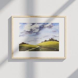 Può includere: Dipinto paesaggistico ad acquerello di dolci colline verdi sotto un cielo nuvoloso. L'opera è incorniciata in una cornice di legno chiaro con un passe-partout bianco. Le iniziali dell'artista, "AE", sono in basso a destra.