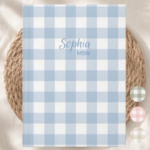 May include: A rectangular notebook featuring a light blue and white gingham check pattern. The center of the cover displays the name Sophia in a blue script font, with the initials MSW printed in a smaller, sans-serif blue font below it.