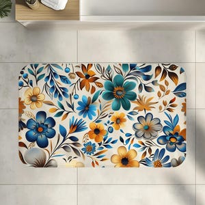 May include: A rectangular bath mat featuring a floral pattern. The design includes blue, teal, and yellow flowers with brown and blue leaves on a cream background. The mat is placed on a tiled floor.