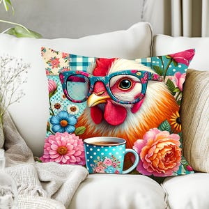 Op de afbeelding: Een decoratief sierkussen met een grillige kip met een bloemenbril. Het kussen heeft een bloemen- en stippenpatroon met een bijpassende koffiemok. Het ontwerp bevat roze, blauwe en oranje bloemen.