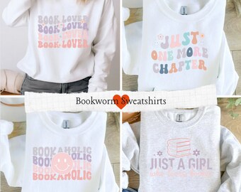 Pode incluir: Quatro camisolas com designs com tema de livros. As camisolas são brancas e cinzentas. Uma diz "BOOK LOVER" em cores pastel, outra diz "JUST ONE MORE CHAPTER", uma terceira diz "BOOKAHOLIC" e a última diz "JUST A GIRL who loves books".
