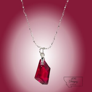 Może przedstawiać: Srebrny łańcuszek z fasetowanym, ciemnoczerwonym kryształowym wisiorem.