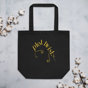 May include: Black tote bag with a gold design that says "plot twist" in a curved font.