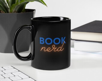 Puede incluir: Taza de cerámica negra con un diseño azul "BOOK nerd". El texto "nerd" está en naranja.