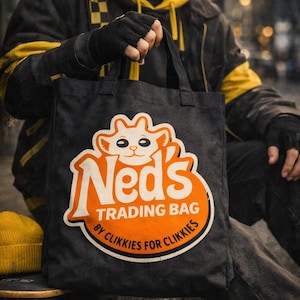 Op de afbeelding: Zwarte draagtas met de tekst "Neds Trading Bag" en een cartoon kat logo in oranje en wit. De tas heeft ook de tekst "By Clikkies for Clikkies" en "Carry Yourself - By Clikkies for Clikkies".