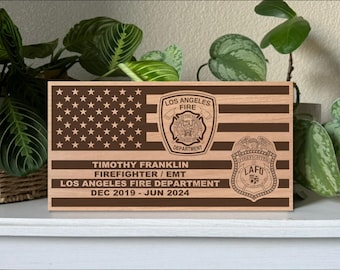 Puede incluir: Una placa de madera con un diseño de bandera estadounidense marrón y blanco. La placa presenta el logotipo del Departamento de Bomberos de Los Ángeles y el texto "Timothy Franklin Bombero/EMT Departamento de Bomberos de Los Ángeles Dic 2019 - Jun 2024".