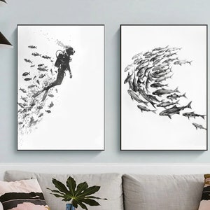 Op de afbeelding: Twee zwart-witte ingelijste prints van onderwaterscènes. De linker print toont een duiker die door een school vissen zwemt. De rechter print toont een school vissen die in een cirkel zwemt.