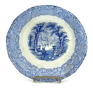 May include: A blue and white porcelain plate with a decorative border and a central image of a building in a landscape.