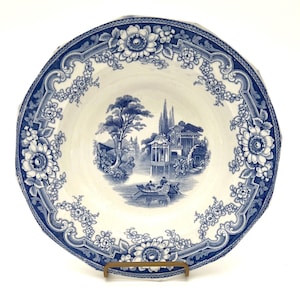 May include: A vintage blue and white porcelain soup bowl with a floral border and a scene of a Chinese garden with a boat on a lake.