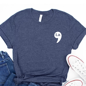 May include: A navy blue t-shirt with a white graphic of a semicolon and the word "La" on the left chest.