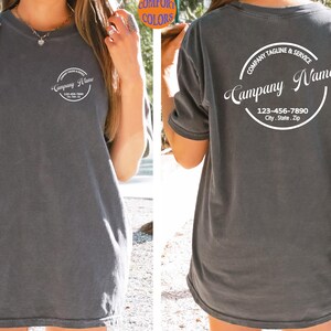 May include: A dark gray t-shirt with a white circular logo on the front and back. The front logo says "Company Name" and the back logo says "Company Tagline & Service" and "Campany Name" with a phone number and address.
