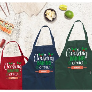 May include: Three Christmas-themed aprons in red, navy blue, and green with the text "Cooking Baking Crew" and a space for a name. The aprons have a pocket and a rolling pin graphic.