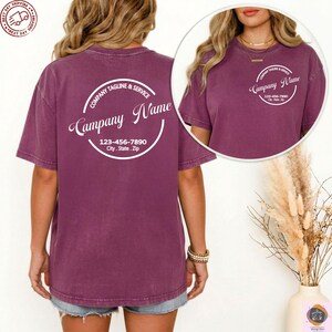 May include: A maroon t-shirt with a white circular design on the back that reads "Company Name", "Company Tagline & Service", and a phone number and address. A smaller version of the design is on the front. The shirt is short-sleeved.