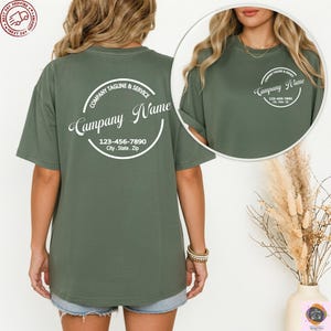 May include: Olive green t-shirt with a circular logo on the back that reads "Company Name" and includes a phone number and address. The shirt has short sleeves and a crew neck. The same logo is on the front of the shirt.