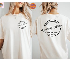May include: Cream-colored t-shirt with a circular logo on the front and back. The logo includes the text "Company Name," "Company Tagline & Service," and a phone number and address. The shirt is a Comfort Colors brand.