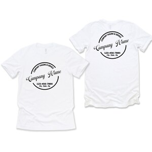 Op de afbeelding: Twee witte t-shirts met een zwart cirkelvormig ontwerp. Het ontwerp bevat de woorden "Company Tagline & Service" en "Company Name" in een scriptlettertype, samen met een telefoonnummer en adres.