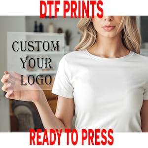 May include: A clear, rectangular sheet with the text "CUSTOM YOUR LOGO" in black, held in front of a white t-shirt. The words "DTF PRINTS" and "READY TO PRESS" are in red at the top and bottom of the image.