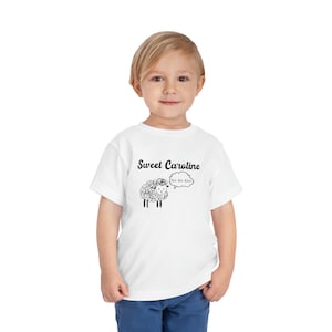 May include: White t-shirt with a black and white illustration of a sheep with a speech bubble that says "BA-BA-BAA" and the text "Sweet Caroline".