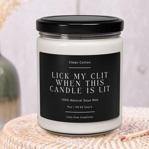 May include: A white candle in a glass jar with a black lid. The black label reads "LICK MY CLIT WHEN THIS CANDLE IS LIT" in white text. The candle is 9oz and made with 100% natural soya wax.