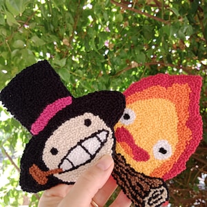 Könnte beinhalten: Zwei handgefertigte, gestickte Aufnäher mit Charakteren aus einem beliebten Zeichentrickfilm. Ein Aufnäher zeigt eine Figur mit schwarzem Zylinderhut und rosa Band. Der andere Aufnäher ist eine Flamme mit Gesicht in Rot-, Orange- und Gelbtönen.