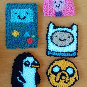 Può includere: Cinque toppe di feltro colorate che rappresentano personaggi della serie televisiva animata Adventure Time. Le toppe raffigurano Finn l'umano, Jake il cane, la principessa Bubblegum, BMO e il re Ghiaccio.