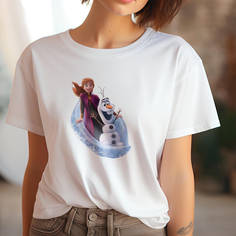 May include: White t-shirt with a graphic print of Elsa and Olaf from the movie Frozen. Elsa is wearing a purple dress and Olaf is wearing a carrot nose.