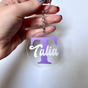 May include: A purple letter T with the name Talia written in white on a clear acrylic keyring.