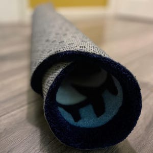 May include: A rolled up rug with a blue and white pattern. The rug has a dark blue border.