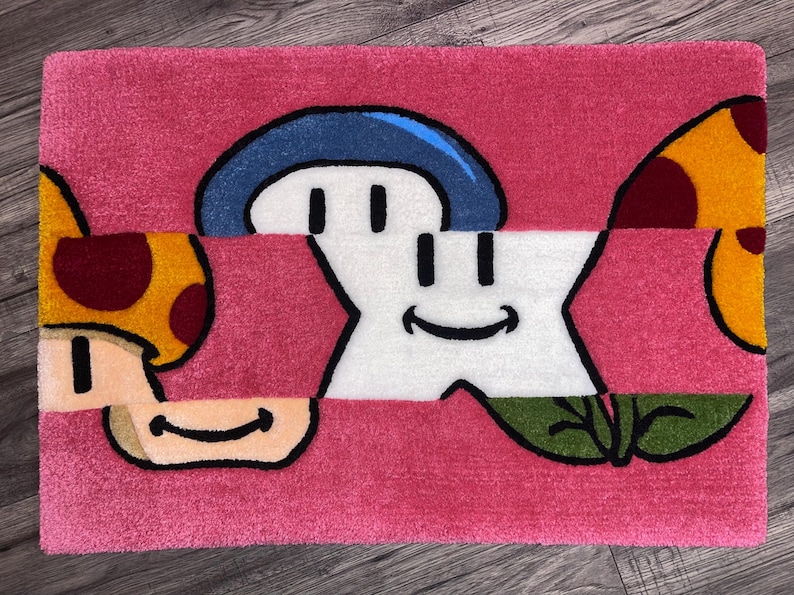 Puede incluir: Una alfombra rosa con una estrella blanca, un hongo azul, un hongo amarillo y una hoja verde. La estrella y los hongos tienen caras sonrientes.
