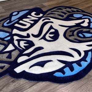 May include: A blue and white rug with a cartoon ram's head and the text "UNC" on it.