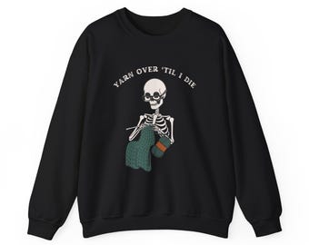 May include: Black sweatshirt with a skeleton knitting a green and brown scarf. The text "YARN OVER 'TIL I DIE" is printed on the sweatshirt.