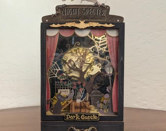 May include: A wooden Halloween-themed shadow box with the text "Night Specter" and "Dark Castle". The box features a spooky scene with a tree, a ghost, and a graveyard. Red curtains frame the scene.