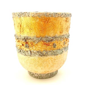 May include: A textured, handcrafted ceramic vase with a unique, layered design. The vase features a warm color palette of yellow, orange, and gray, with a rough, bark-like texture around the rim and midsection. The base is a light beige.